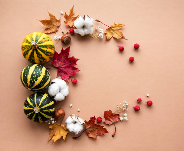 Autumn decoration with pumpkins and dry maple leaves in the shape of a circle on a brown background - Photo, Image