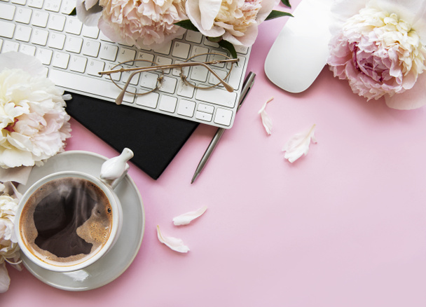 フラットレイアウト花と女性のオフィスの机の上を表示します。ラップトップ、花の牡丹、アクセサリー、ノートブック、眼鏡、ピンクの背景にコーヒーカップを持つ女性のワークスペース。休日の背景コピースペース - 写真・画像