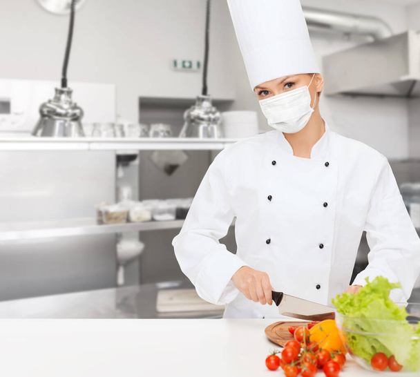 female chef in mask cutting vegetables at kitchen - Foto, imagen