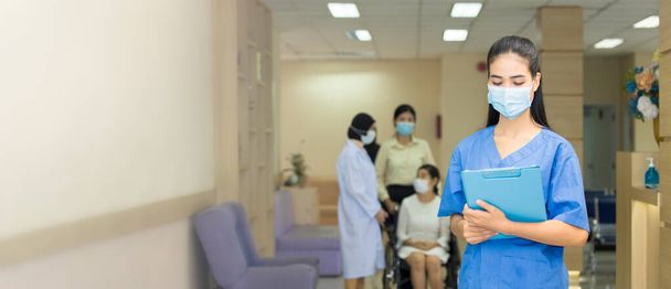 Female Medical personnel or Doctor wearing face masks and holding the patient's treatment file standing in the corridor while the back is the atmosphere inside the hospital was full of people. - Photo, Image