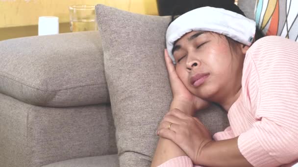 Une femme malade a mis une serviette mouillée sur son front pour soulager les maux de tête de fièvre et la toux couchée sur un canapé à la maison. Soins de santé et médicaux. - Séquence, vidéo