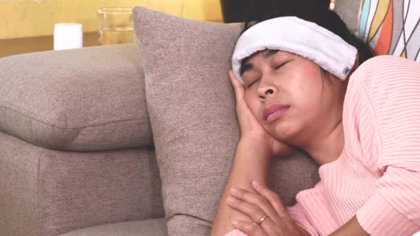 Zieke vrouw legde een natte handdoek op haar voorhoofd om de koorts te verlichten hoofdpijn met een zere keel liggend op een bank thuis. Gezondheidszorg en medische zorg. - Video