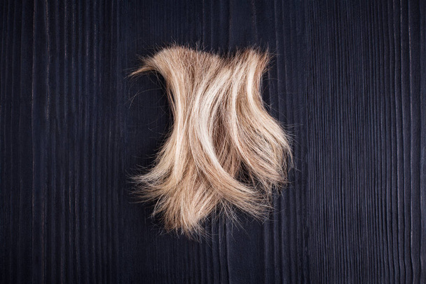 Blond faliste włosy zamek czarny drewniane tło zbliżenie, odciąć naturalne blond włosy curl na ciemnym drewnie, fryzura, fryzura, ludzki strzyżenie włosów, strzyżenie, strzyżenie, fryzura, coiffure, fryzjer, przestrzeń kopiowania - Zdjęcie, obraz