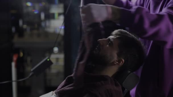 Coiffeur couvre le visage du jeune homme barbu avec une serviette chaude avant de se raser - Séquence, vidéo