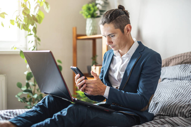 Un homme d'affaires en costume travaille à distance sur un ordinateur portable au lit à la maison. S'adapter au travail en cas de pandémie - Photo, image