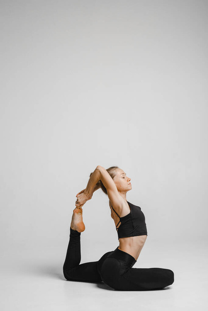 Woman in black bodysuit doing stretching yoga pose - Φωτογραφία, εικόνα
