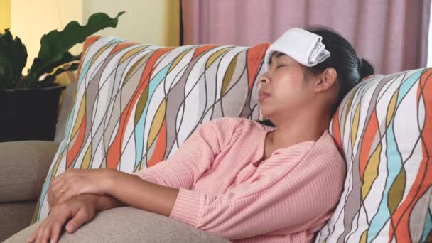 Sairas nainen laittaa märkä pyyhe otsaansa lievittää kuumetta päänsärkyä ja yskä makaa sohvalla kotona. Terveydenhuolto ja lääketiede. - Materiaali, video