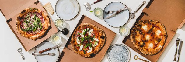 Pizza party for friends or family. Flat-lay of pizzas in boxes, lemon drinks and cutlery over plain white table background, top view. Fast food, comfort food, Italian cuisine concept - 写真・画像