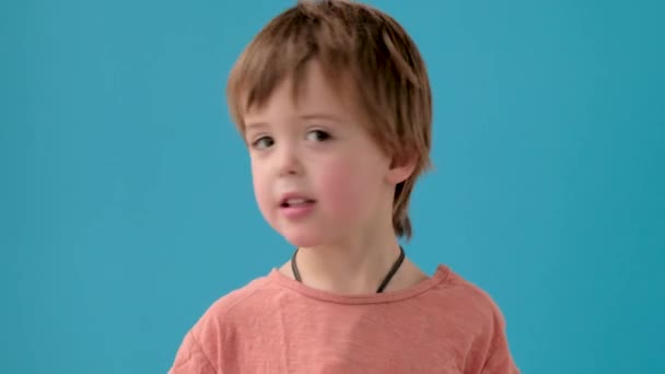 Pequeño niño sacude la cabeza en incredulidad a la pared de color turquesa brillante - Metraje, vídeo
