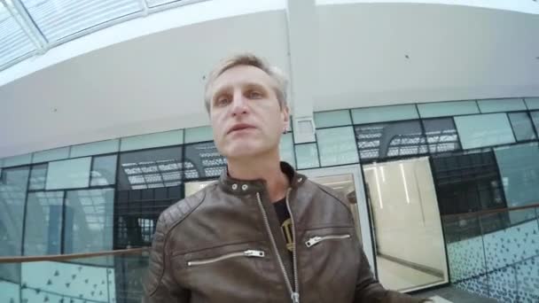 Muž cestující mluví na kameru při chůzi v moderní budově - Záběry, video