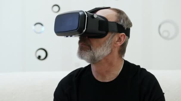 Modern középkorú férfi szürke szakállal VR headsetet használ, körülnéz. - Felvétel, videó