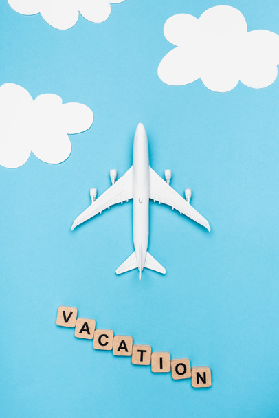 top view of plane model and cubes with word vacation on blue sky background - Fotografie, Obrázek