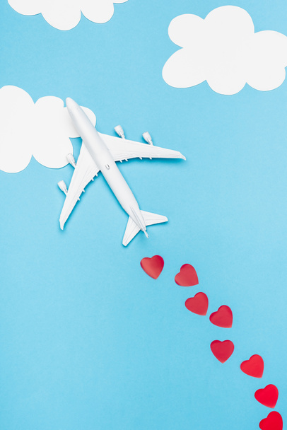 top view of plane model and red hearts on blue background with white clouds - Фото, изображение
