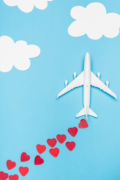 top view of plane model and red hearts on blue background with white clouds - Fotó, kép