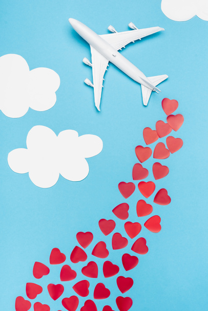 top view of plane model and red hearts on blue background with white clouds - Fotoğraf, Görsel