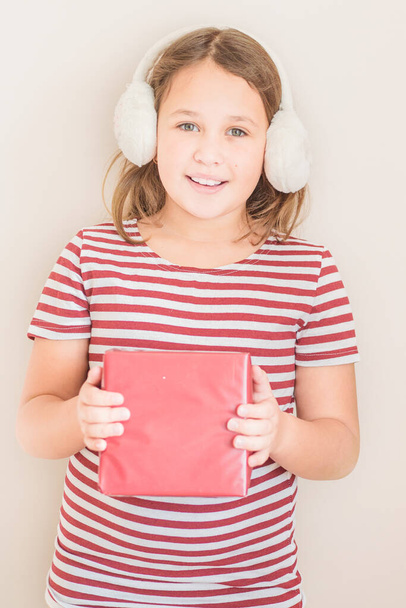 Mädchen in rot-weiß gestreiftem T-Shirt mit Ohrenschützern aus Fell mit Geschenk - Foto, Bild