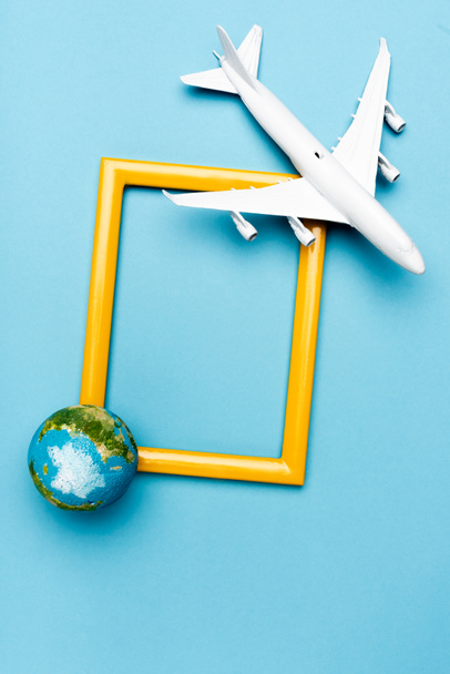 top view of white plane model, globe and empty frame on blue background - Fotografie, Obrázek