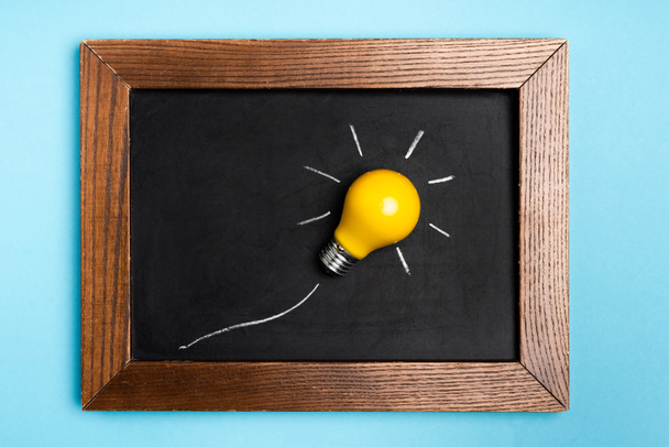top view yellow light bulb and chalkboard on blue background - Photo, Image