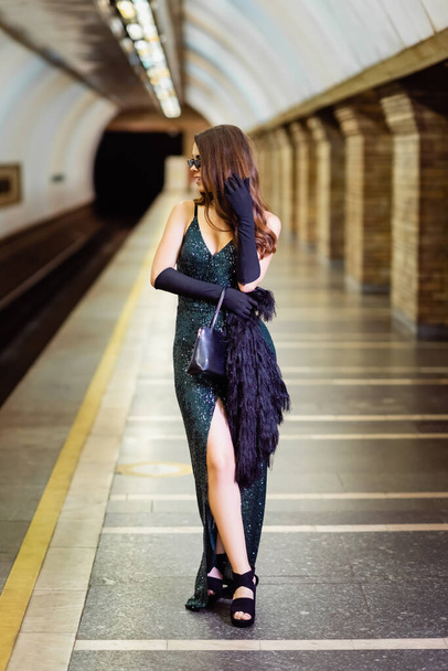 μοντέρνα γυναίκα σε μακρύ μαύρο φόρεμα στέκεται στην πλατφόρμα του μετρό - Φωτογραφία, εικόνα