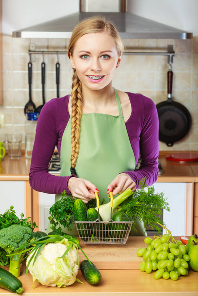 Buying healthy dieting food concept. Woman in kitchen having many green vegetables holding small shopping basket. - Foto, Imagen