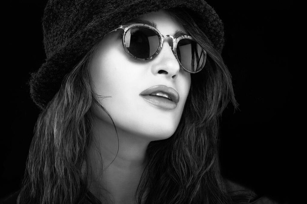 Monokróm gyönyörű elegáns fiatal nő barna haj visel divatos napszemüveg és egy fekete kalap egy közeli kivágott portré ajkak elválasztva néz oldalra, mint a fekete copyspace - Fotó, kép