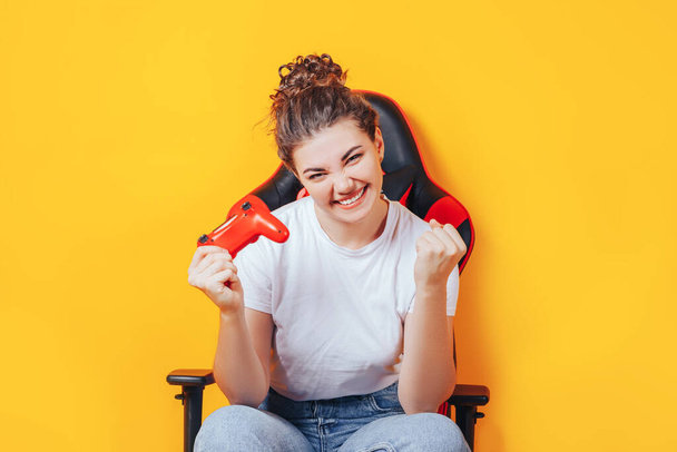 Όμορφη νεαρή γυναίκα που παίζει βιντεοπαιχνίδια ενώ κρατά χειριστήριο παιχνιδιών ενώ κάθεται στην καρέκλα τυχερών παιχνιδιών. Γυναίκα στα eSports. Θέση για κείμενο - Φωτογραφία, εικόνα