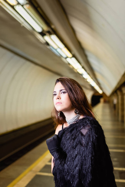 glamour woman in faux fur jacket looking away while standing on underground platform - Foto, Imagem