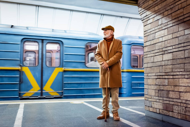 vanha mies syksyllä asu seisoo kävelykeppi metroasemalaiturilla lähellä junaa - Valokuva, kuva