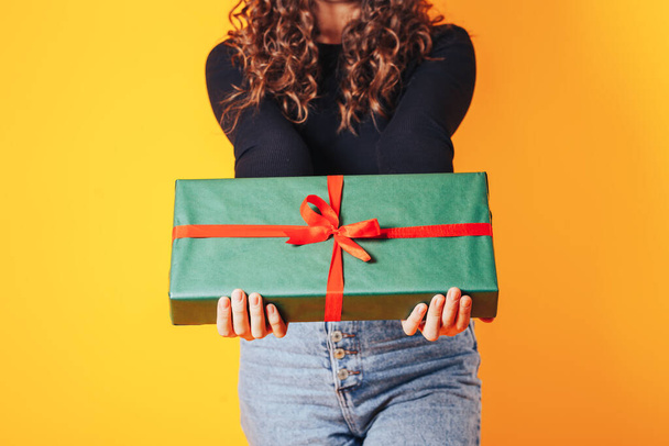 Γυναίκα που κρατάει ένα μεγάλο κουτί στα χέρια της. Δώρο σε πράσινη συσκευασία με κόκκινη κορδέλα και κόκκινο φιόγκο. Δώρο για γυναίκα για διακοπές ή ειδική περίσταση - Φωτογραφία, εικόνα