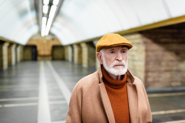 oudere man in herfstpet en jas bij metrostation - Foto, afbeelding