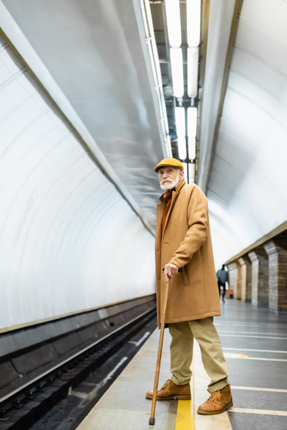 elderly man in autumn outfit standing on underground platform with walking stick - Photo, Image