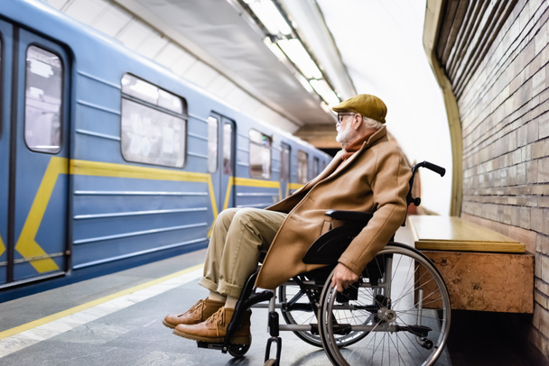 homme handicapé âgé en fauteuil roulant, vêtu de vêtements d'automne, près du train sur le quai du métro - Photo, image