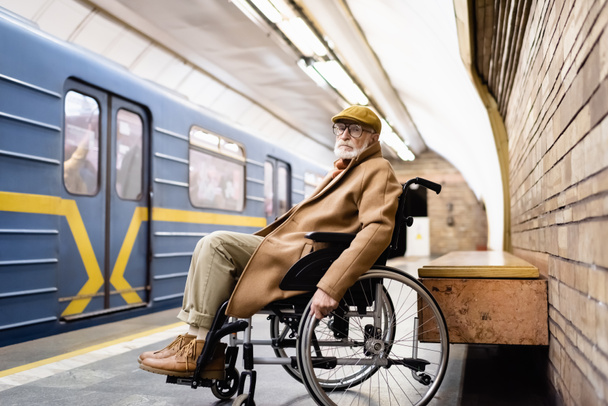 ηλικιωμένος ανάπηρος σε αναπηρική καρέκλα, φορώντας φθινοπωρινή στολή, κοντά στο τρένο στην πλατφόρμα του μετρό - Φωτογραφία, εικόνα