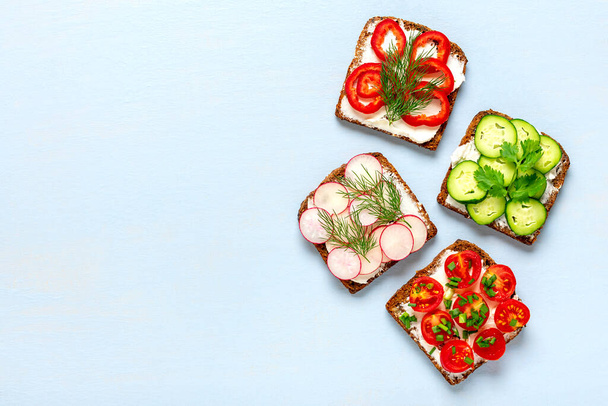 Variety of sandwiches for breakfast - slice of whole grain dark bread, pepper, cream cheese, cucumbers, radishes, cherry tomatoes, garnished with dill, green onions on blue table Top view Flat lay - Photo, Image