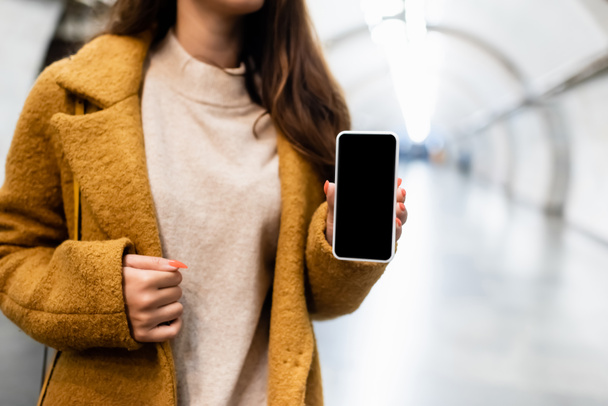 częściowy widok kobiety w jesiennych ubraniach pokazuje smartfon z pustym ekranem na stacji metra - Zdjęcie, obraz