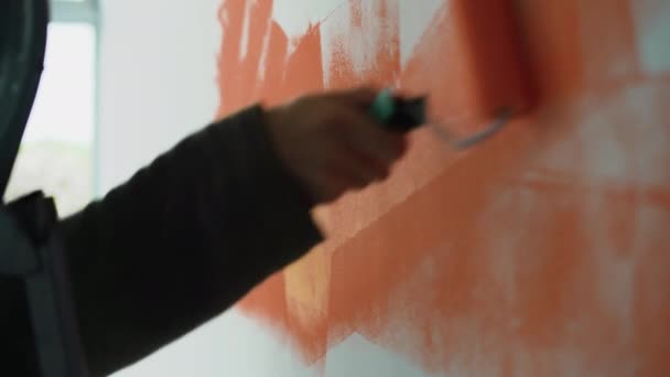 Κοντινό πλάνο ενός ανδρικού χεριού. Βάψτε τον τοίχο με πορτοκαλί χρώμα με ρολό. - Πλάνα, βίντεο