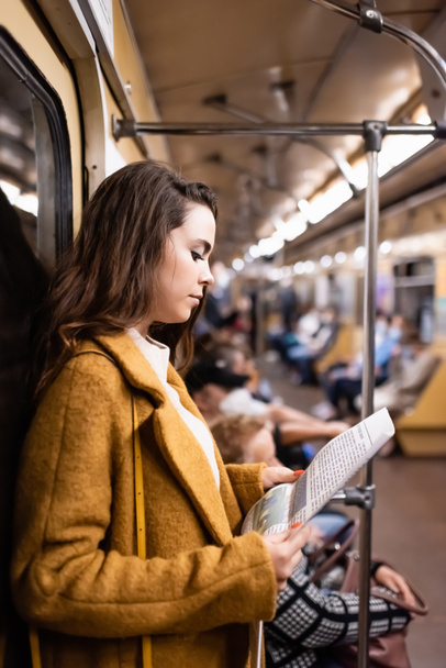 Junge Frau im Herbstmantel liest Zeitung während U-Bahn-Fahrt - Foto, Bild