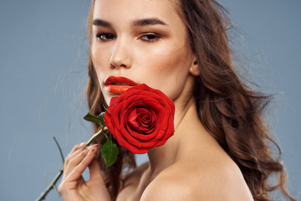 Retrato de una mujer con una rosa roja en sus manos sobre un fondo gris hombros desnudos maquillaje de noche - Foto, imagen