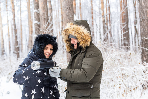 Young couple in love drink a hot drink from a thermos and enjoy winter nature. - 写真・画像