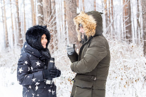 Sezon i koncepcja spaceru - Szczęśliwa para pije gorącą herbatę w zimowym lesie - Zdjęcie, obraz