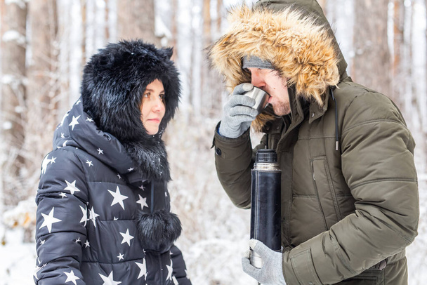 愛の若いカップルは魔法瓶から熱い飲み物を飲み、冬の自然を楽しむ. - 写真・画像