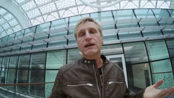 Férfi utazó beszél a kamera, miközben séta a modern épületben - Felvétel, videó