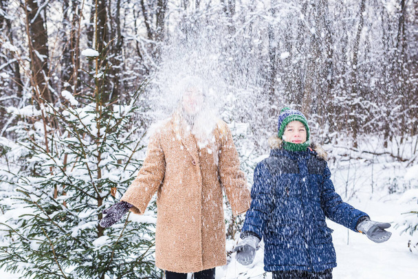 Szülői, szórakoztató és szezon koncepció - Boldog anya és fia szórakozás és játék hó téli erdőben - Fotó, kép