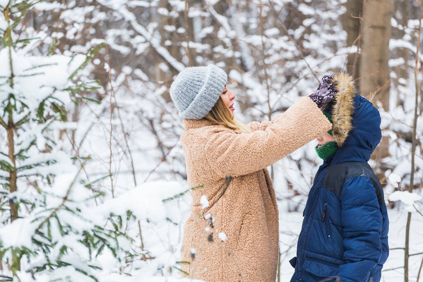 Portrait of happy mother with child son in winter outdoors. Snowy park. Single parent. - Photo, Image