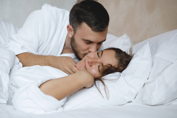 Two in bed. A bearded man kisses a sleeping woman. - 写真・画像