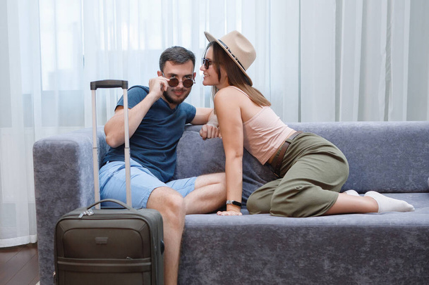 Dos amantes en gafas de sol y sombreros se están divirtiendo en el sofá. Descanso en el hotel, turistas de viajes. - Foto, Imagen