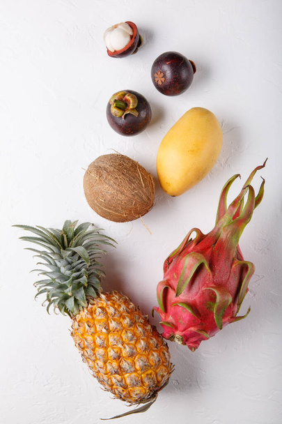 白い熱帯果実。ドラゴンフルーツ、マンゴー、パイナップル、マンゴスチン、バナナ、ココナッツ。健康的な食べ物の背景。夏のコンセプト。トップビュー、フラットレイアウト. - 写真・画像