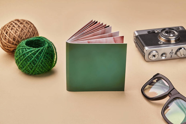 Yeşil kapaklı fotoğraf kitabı, eski model kamera, gözlükler ve bej renkli arka planda iki renkli jüt sicim. Kapat, boşluğu kopyala - Fotoğraf, Görsel