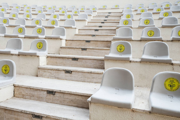 Rows of seats in amphitheater with warning sign for for social distancing during coronavirus outbreak. New normal lifestyle in world pandemic. Keeping safe distance between guests for performance. - Photo, Image