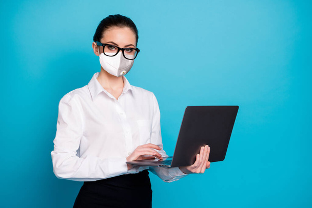 Portrait of nice attractive skilled serious smart lady holding in hands laptop wear mask isolated over vibrant blue color background - 写真・画像